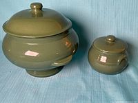 Large and small green ceramic pots with lids displayed side by side