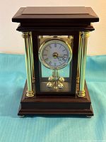 Front view of wood and glass mantel clock with white dial and brass-tone columns