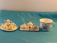 Both miniature tea sets on blue cloth with standard teacup for scale
