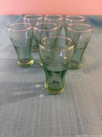 Front view of seven green miniature Coca-Cola glasses