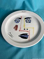 Front view of decorative plate showing full abstract face design and signatures