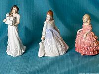 Front view of three Royal Doulton figurines on blue fabric backdrop