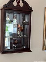 Front view of wall-mounted curio cabinet showing glass door, mirrored back, interior shelves