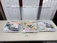 Three clear plastic storage cases open, filled with assorted crafting supplies