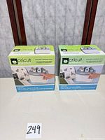Two boxed Cricut Jukebox units on table, lot number card visible
