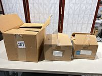 Three cardboard boxes containing stacks of kraft chipboard envelopes