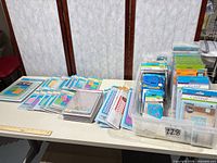 Wide view of table with 30+ sealed embossing folders & dies in blister packs