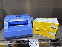 Blue Xyron 5" Creative Station model 500 with two yellow refill cartridge boxes