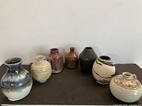 All seven small studio pottery vases front view