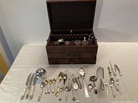 Overall lot showing Birks chest open with contents and array of flatware and serving pieces on table