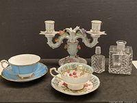 Group shot of all items: two cup-saucer sets, candelabra, perfume bottle, decanter