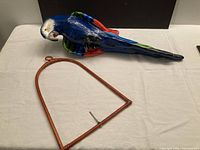 Parrot sculpture and separate arched perch laid on table