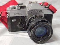 Front angled view of camera showing Canon FTb branding, attached FD lens, red strap