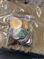 Clear plastic bag containing a variety of round pinback buttons with different colors and text