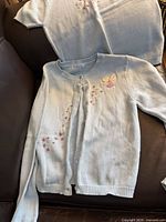 Cardigan and part of second garment showing embroidery and ruffle trim