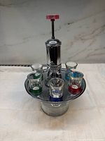 Full view of chrome and glass liquor dispenser with six shot glasses in tray
