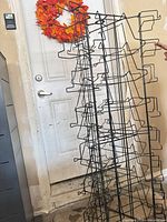 Full view of tall black wire display rack leaning against wall