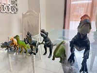 All seven dinosaur figures lined up on glass table