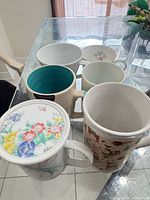 Group of six cups on glass table, showing exterior prints and turquoise interior