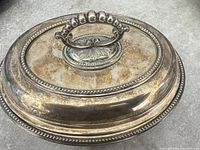 Lidded silver-plated serving dish showing ornate handle and beaded border