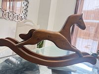 Full left-side view of wooden rocking horse on glass table