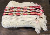 folded crochet blanket showing cream body and striped fringe