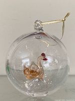 Full view of clear glass ball ornament showing internal swan and hanging cord