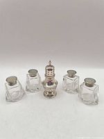 Group shot of four glass salt shakers and one sterling pepper castor
