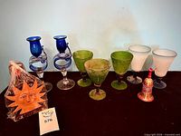 All items lined up: blue candleholders, green goblets, frosted goblets, wooden sun candleholder in plastic, painted wooden bell