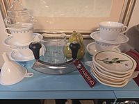 Group shot of entire lot showing plates, Corelle cups/saucers, measuring cup, mezzaluna, funnel, ceramic pear