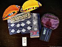 All nine accessories laid out on dark surface: two caps, two bandannas, bell anklets, wallet, change purse, compact backpack visible