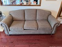 Front view of brown three-seat couch with three cushions and nailhead trim