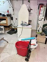 Hamper with iron on lid, red bucket, laundry basket, hand truck visible