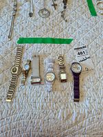 All six wristwatches laid out on quilted surface with MaxSold lot tag