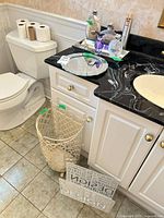 Overview of bathroom accessories on vanity and floor: wastebasket, mirrored tray with glass perfume bottles, wall panels
