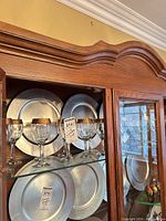 Cabinet view showing multiple wine glasses with gold rims in front of metal chargers