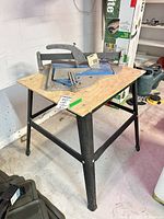 Overall view of metal stand table with plywood top and tile cutter on surface