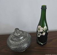 Metal lidded bowl beside painted bottle