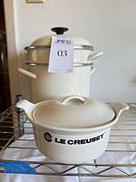 Front view showing Le Creuset casserole in front of white enamel pot with steamer and lid