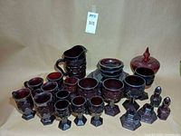 Group shot of entire ruby red glass collection including pitcher, goblets, mugs, plates, compote