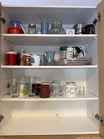 full cabinet view showing three shelves of assorted mugs, glasses, jars, containers