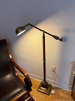 Full view of lamp showing lit shade, adjustable arm, wood column, base