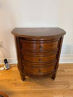 Front view of cherry demi-lune chest showing three drawers, knobs, and legs