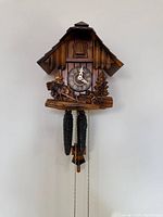 Front view of wooden cuckoo clock showing carved details, dial, weights, and pendulum