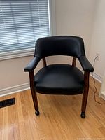 Front view of black faux leather armchair showing wood frame, nailhead trim and casters