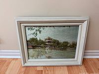 Full view of framed silk embroidery leaning against wall