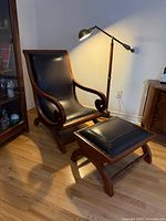 Full view of chair and ottoman showing wood frame, black leather cushions