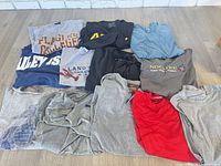 All 12 T-shirts laid out folded, showing colors and graphics