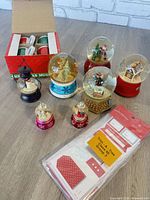 Group shot of seven snow globes, four mugs in box, sealed gift tags