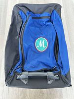 Front view of blue and black rolling duffel suitcase with monogram patch